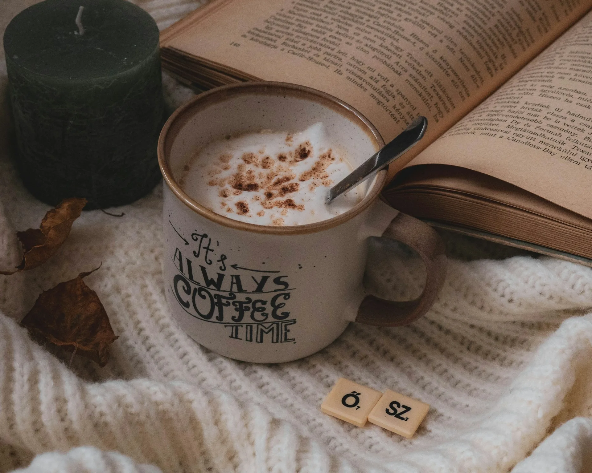 A cup of coffee and a candle on top of a blanket, in front of some cosy fiction - Photo by Sarolta Balog-Major on Unsplash